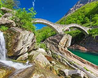 A picturesque stone bridge spans a clear river surrounded by lush greenery.
