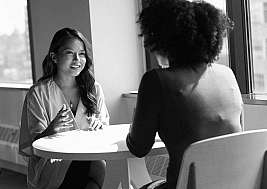 A woman engages in discussion with another at a table.